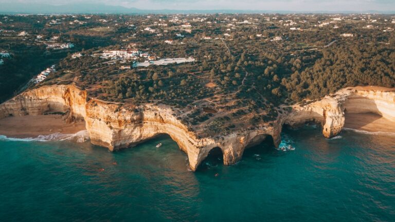 Aerial view of coastal cliffs in Europe with the ocean in the foreground and houses scattered in the distance during sunset.