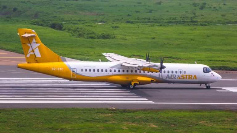 A yellow and white Air Astra airplane taxiing on a runway against a green landscape.