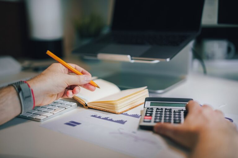 A person analyzing financial data with a calculator and notebook, amid economic updates on a desk.