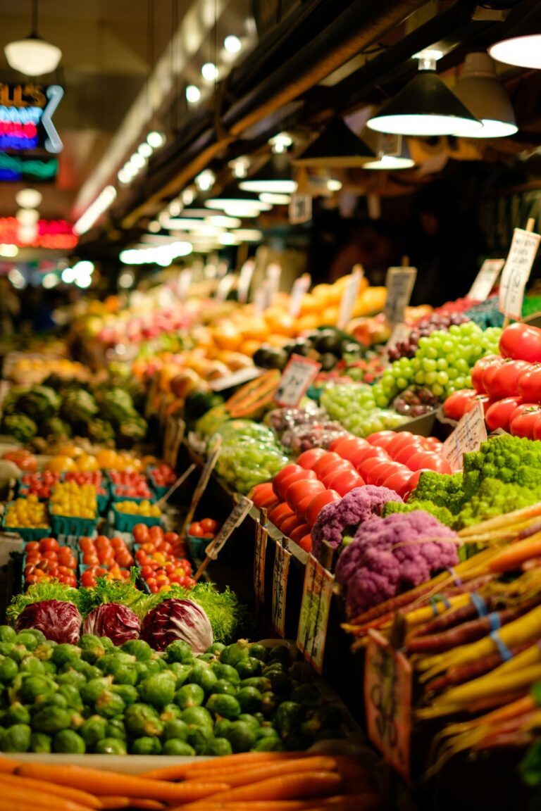 Vibrant assortment of fresh vegetables and fruits displayed at a bustling market stall under bright lights