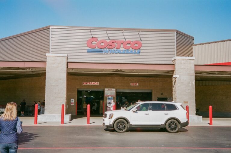 Front entrance of a Costco Wholesale store with customers and vehicles