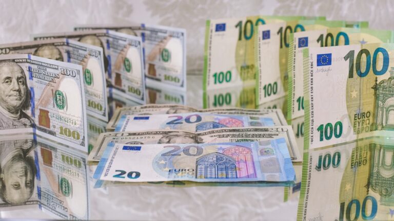 A close-up view of American dollar bills and European euro banknotes arranged on a reflective surface.