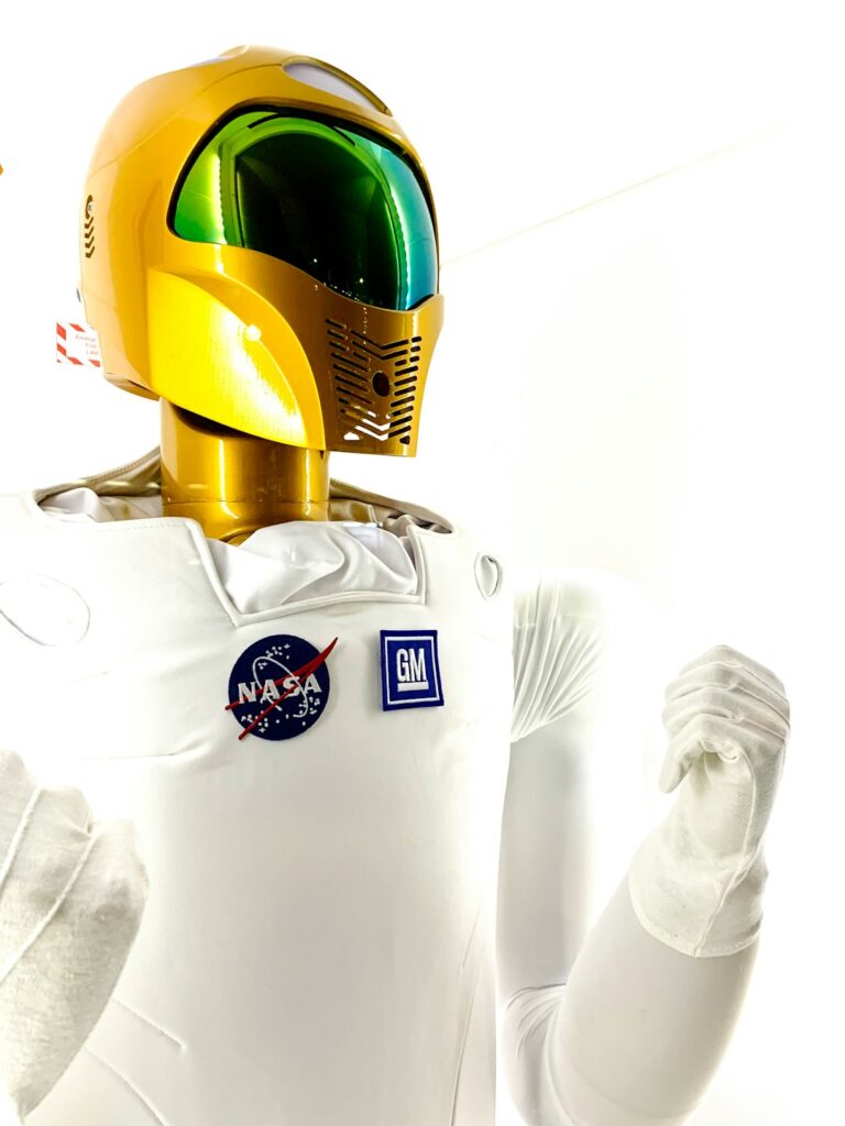 Close-up of a humanoid robot with a gold helmet and white suit featuring NASA and GM logos