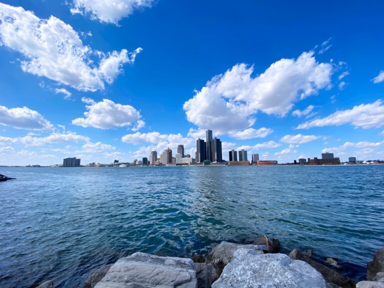 View of Detroit skyline with office buildings against a blue sky and water in the foreground