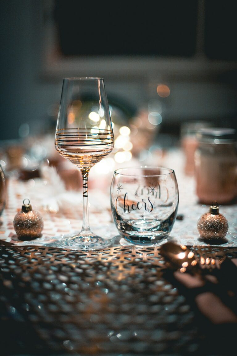 Festive table setting with a decorated wine glass and a "cheers" glass, surrounded by elegant ornaments.