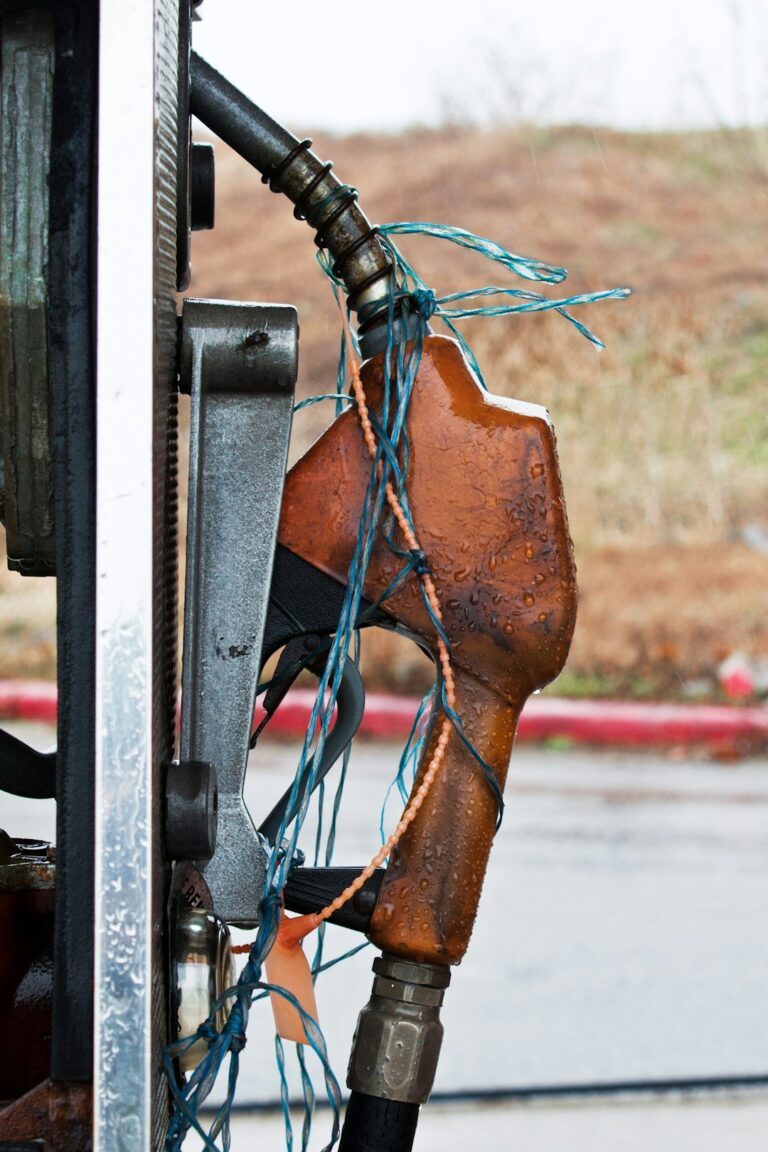 Close-up of a gas pump nozzle with visible raindrops and blue strings tied around it