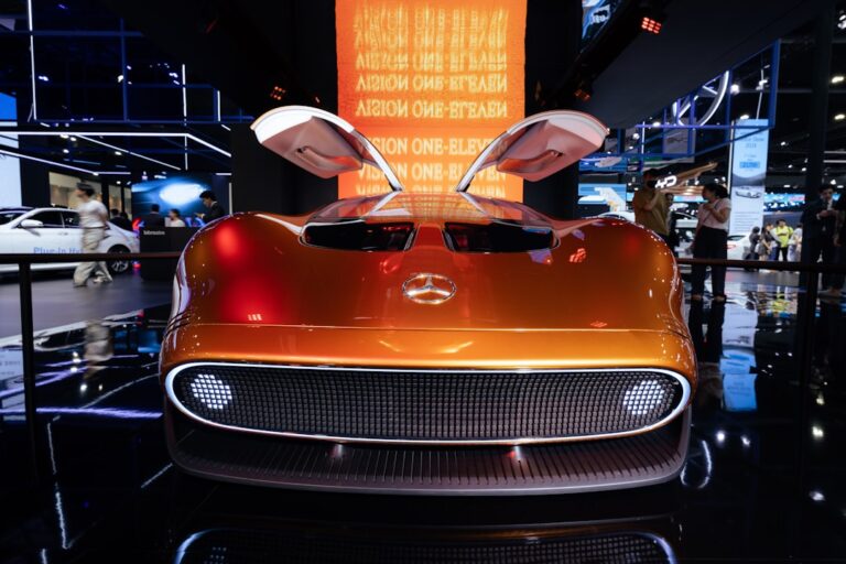 A shiny orange Mercedes-Benz electric concept car with its doors open showcasing futuristic design at an auto show exhibit.