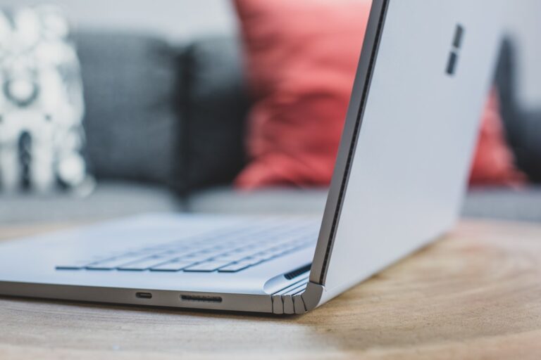Close-up of a Microsoft Surface laptop placed on a wooden table with cushions in the background