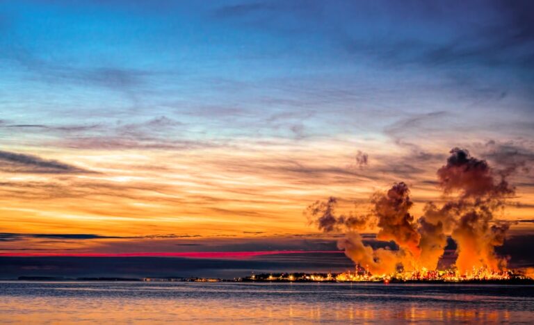 Oil refinery with smoking chimneys at sunset over the water