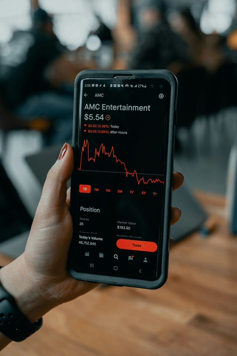 Person holding a smartphone displaying a stock trading app with declining AMC Entertainment stock price