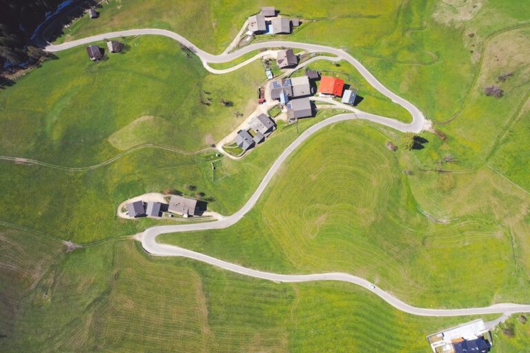 Aerial view of a winding road passing through a serene countryside village with green fields.