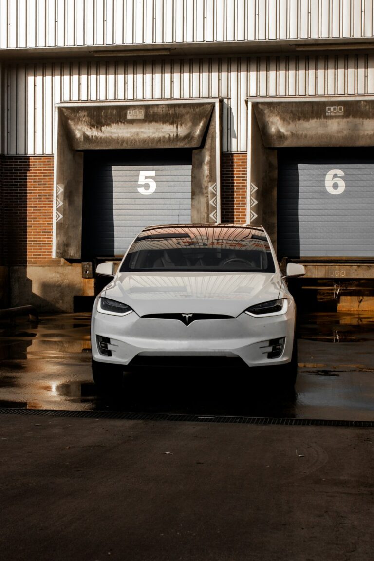 Front view of a white Tesla car parked in front of warehouse doors