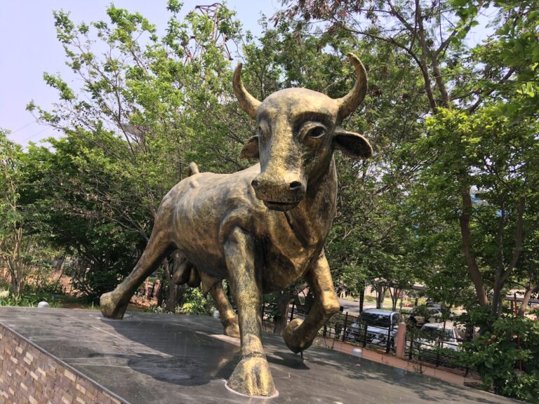 Bronze bull statue symbolizing a bullish stock market trend in a lush garden setting