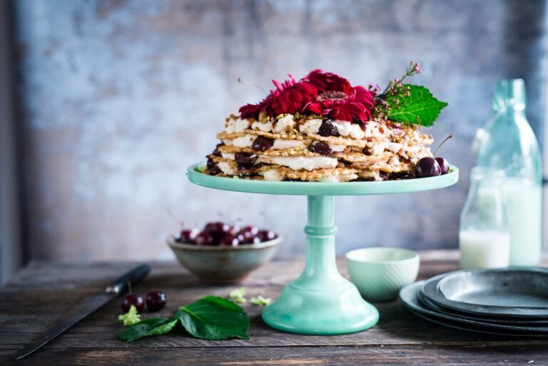 Decorative stack of pancakes topped with fresh cherries and cream on a turquoise cake stand