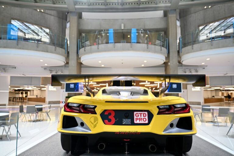 Rear view of the yellow Corvette Racing car inside a modern building, showcasing its sleek design and GTD Pro sticker.