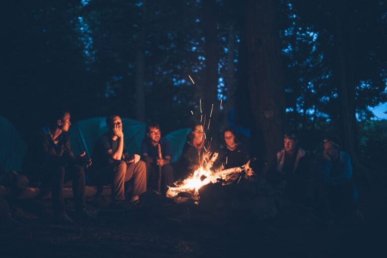 Group of friends sitting around a campfire in the woods during the evening