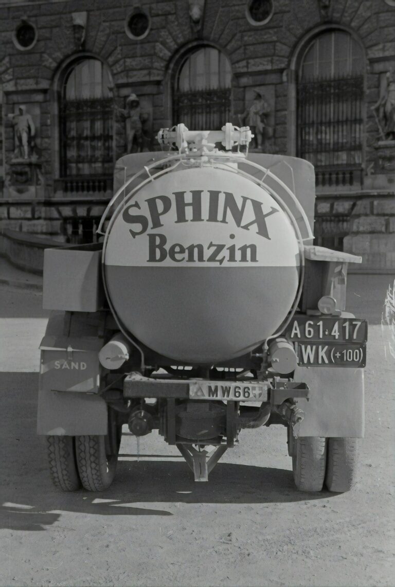 Rear view of an old Sphinx Benzin fuel truck parked in front of a stone building