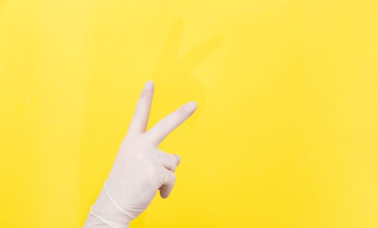 Hand wearing a glove showing a peace sign against a bright yellow background.