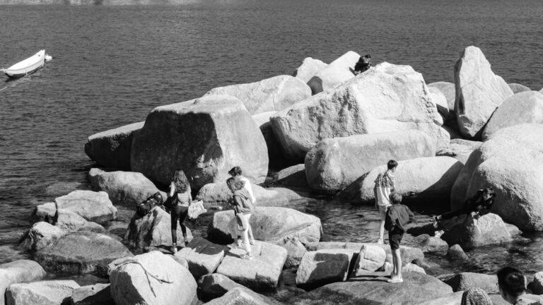 People exploring large rocks by the shoreline during a cloudy day