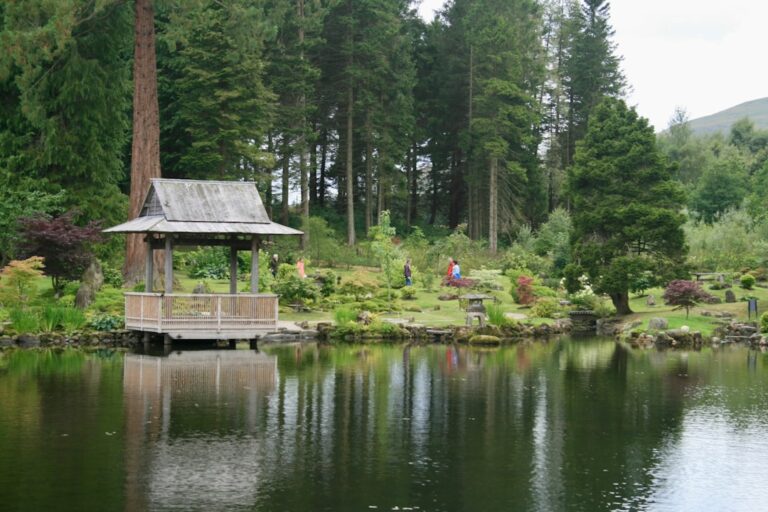 Serene garden with a wooden pavilion by a lake surrounded by trees and greenery