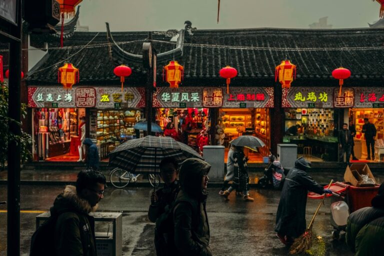 People walking with umbrellas in front of traditional shops at a rainy market in Shanghai, China