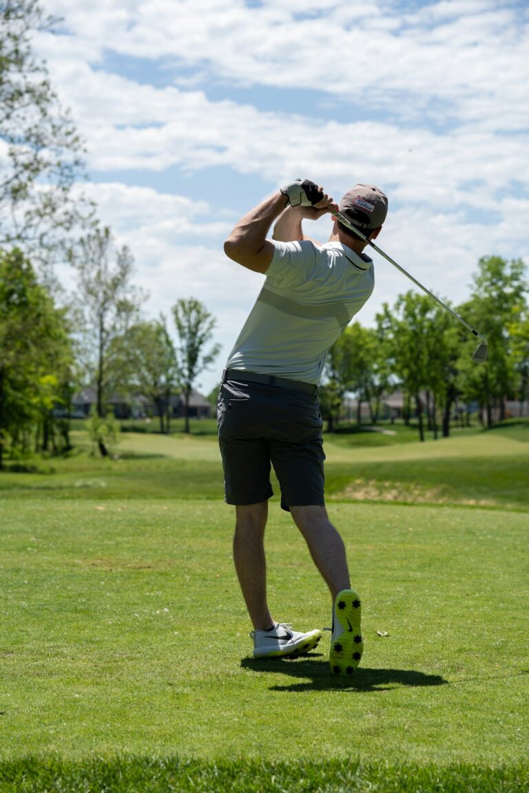 A golfer swinging a club on a bright day at a green golf course