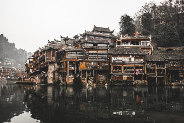 Traditional Chinese buildings on stilts over a river with a misty background