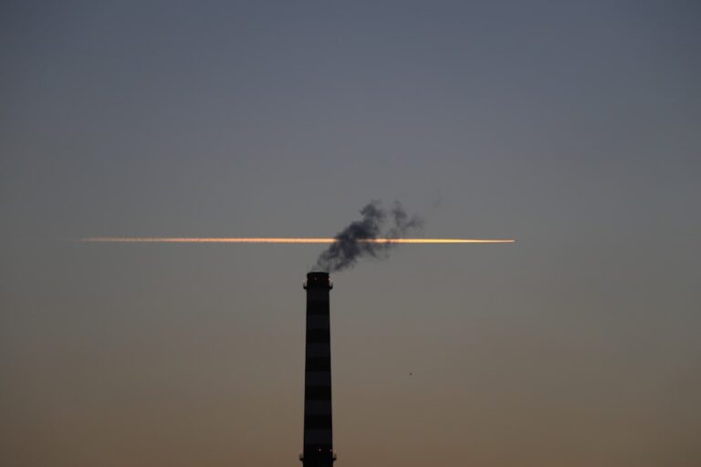 Silhouette of a smokestack with a bright trail in the sunset sky