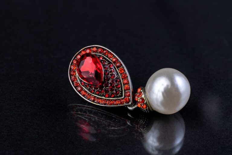 Close-up of an elegant pendant featuring a large red gemstone and pearl on black background