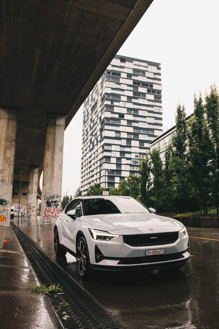 White electric pickup truck parked under a concrete bridge in a modern urban environment with high-rise buildings in the background