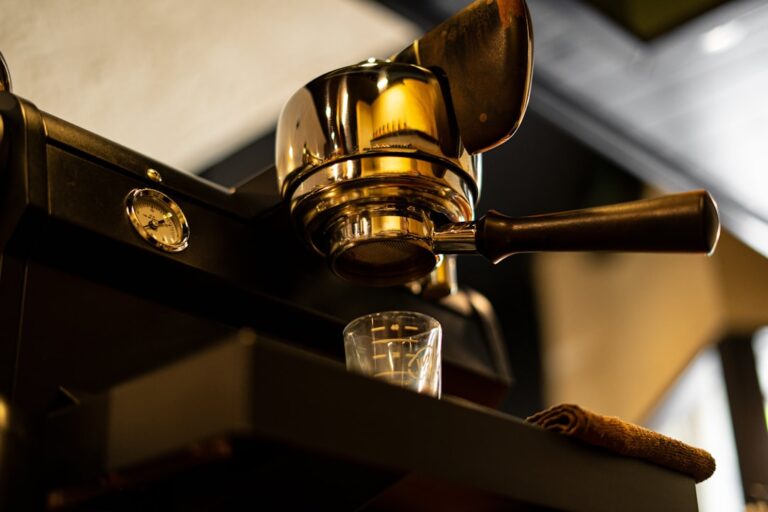 Close-up view of a gleaming espresso machine lever with a small glass placed underneath in a modern cafe.