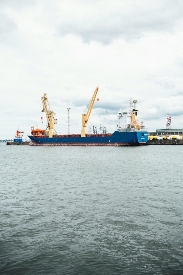 Large oil tanker docked at a port with cranes in the background on a cloudy day