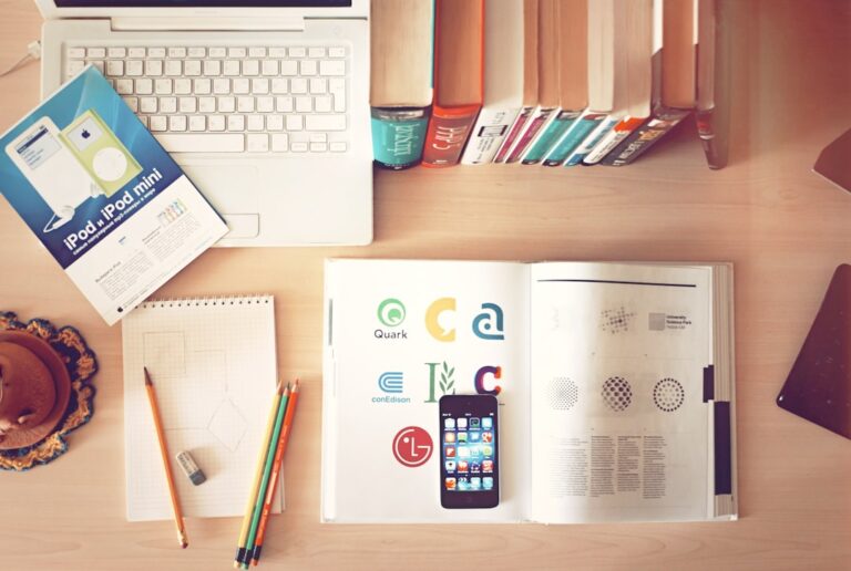 Workspace featuring a variety of office and study tools, including a laptop, books, a mobile phone, a notebook, and colorful pencils.