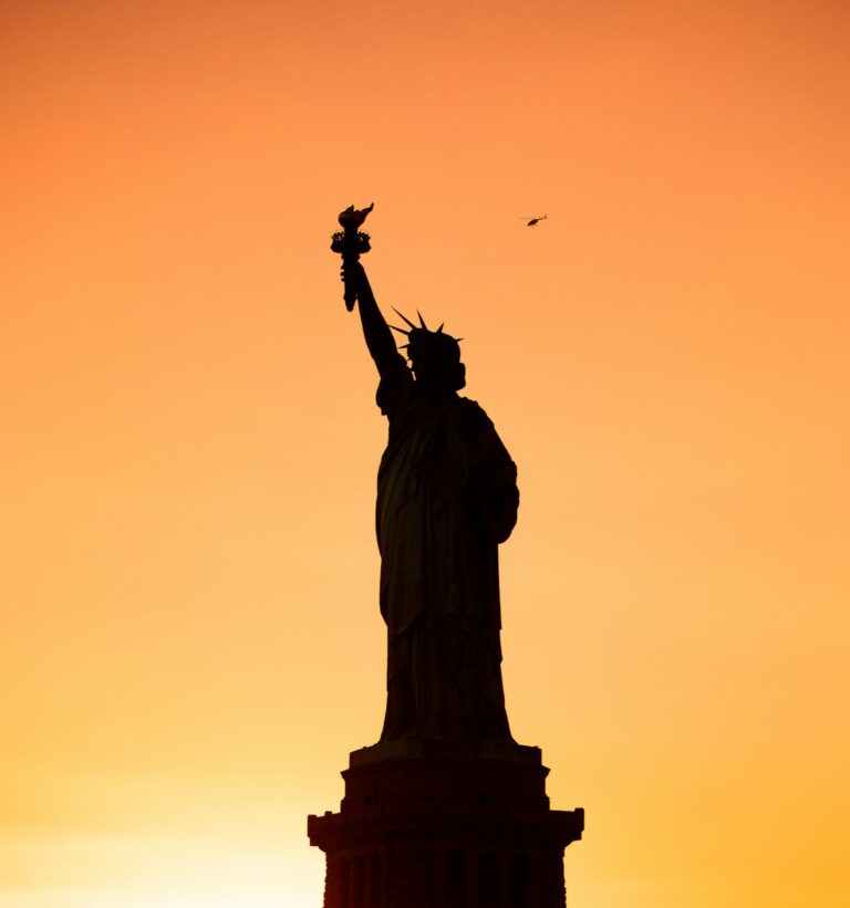 Silhouette of the Statue of Liberty against a vibrant orange sunset sky