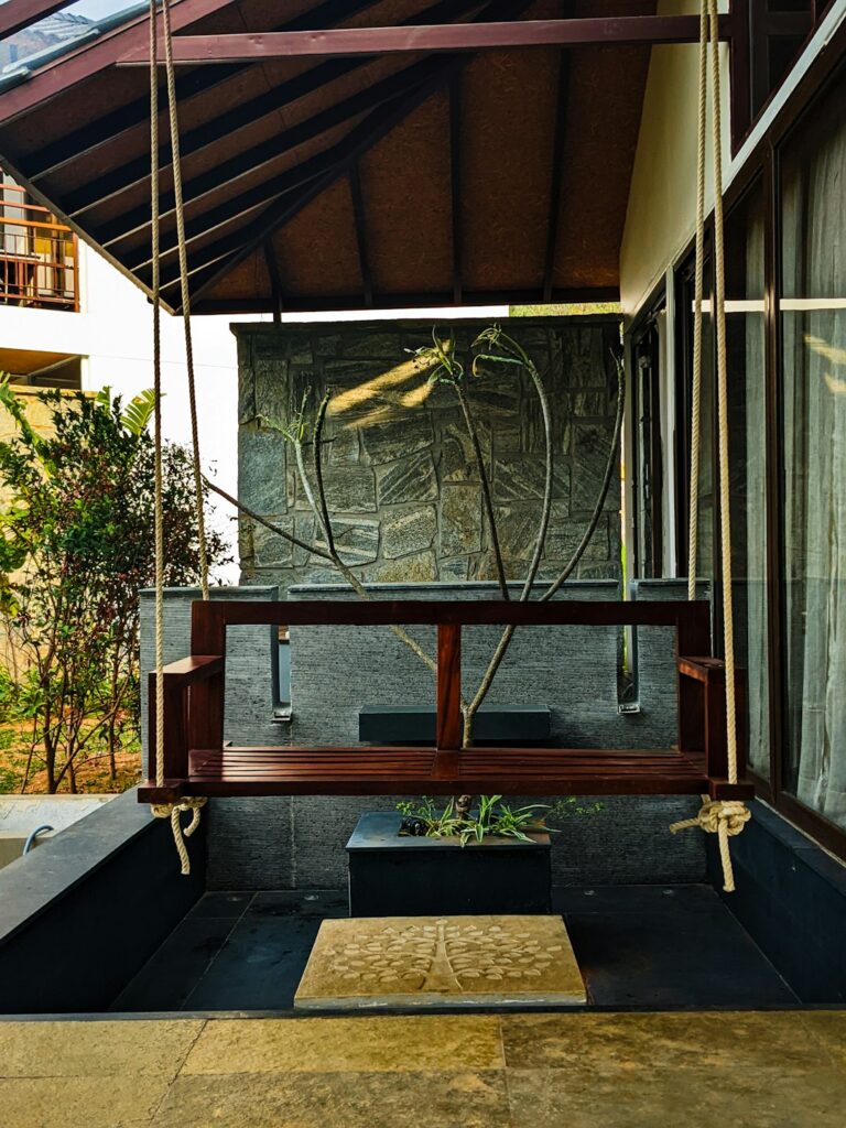 Wooden swing hanging from the ceiling in a modern patio with stone walls and potted plants